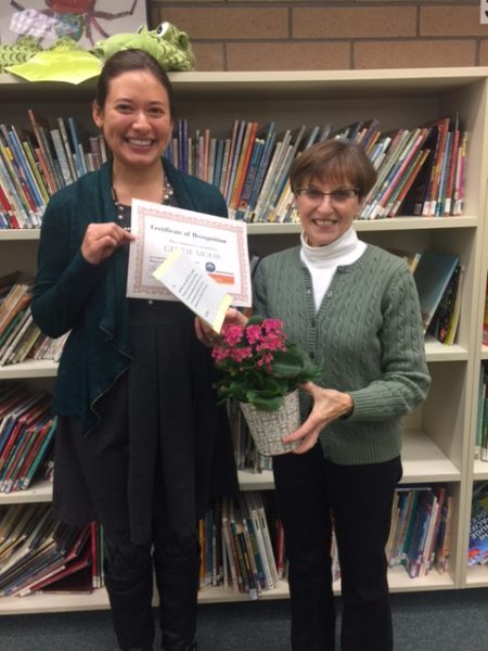 maria and gerrie standing in front of bookshelf with books holding certificate