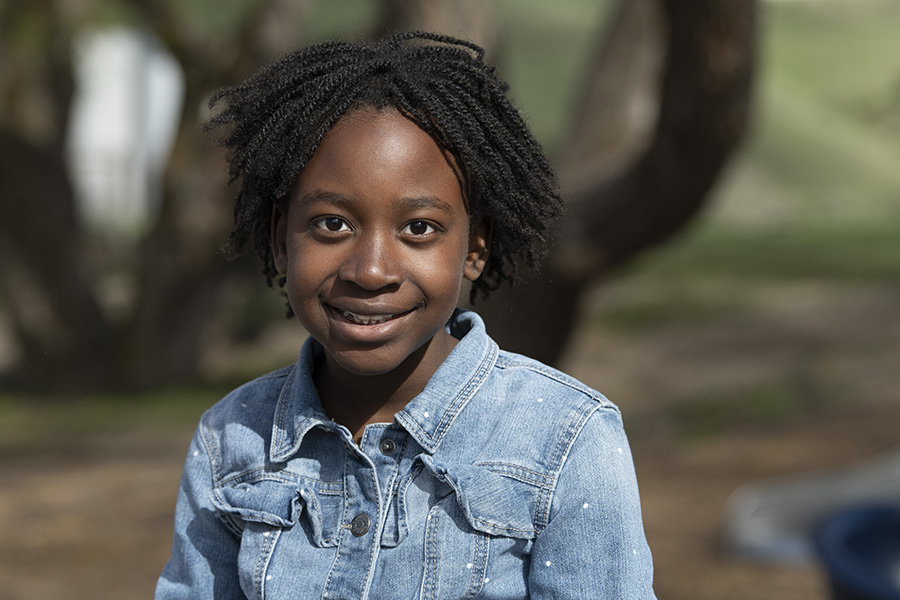 A young girl from Thrive's programs smiles while outside in a park